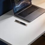 Pióro i laptop na czystym biurku symbolizujące styl pisania człowieka powtórzony przez AI.